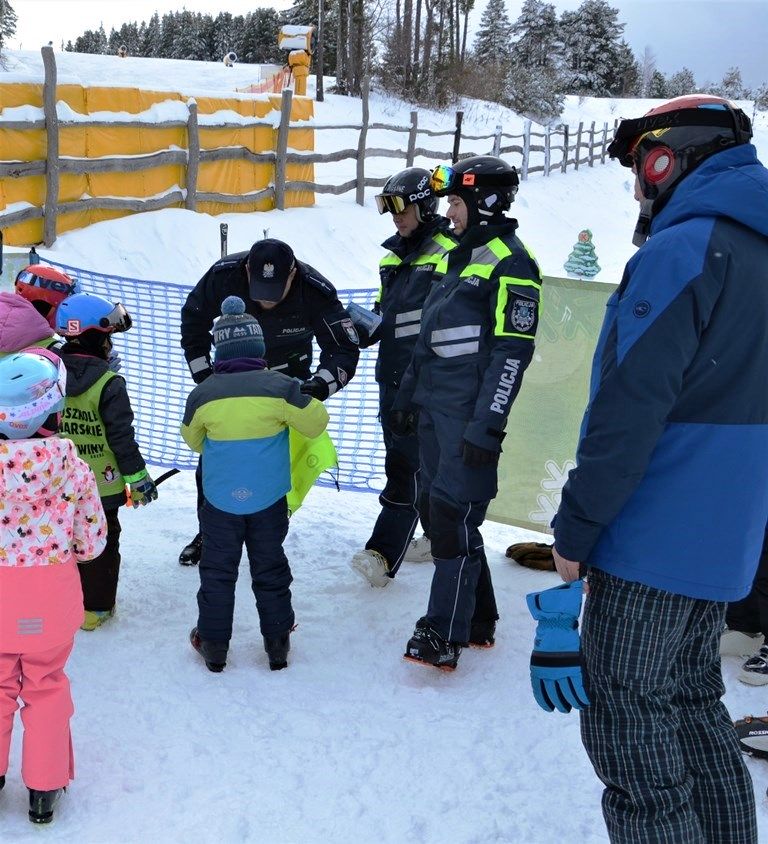 policjant przekazuje chłopcu odblaskową torbę, obok inne dzieci i policjanci z patrolu narciarskiego