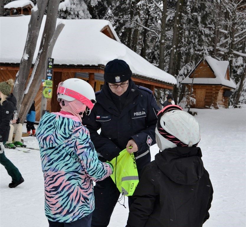 policjant rozmawia z młodymi narciarzami i przekazuje im odblaskowe gadżety
